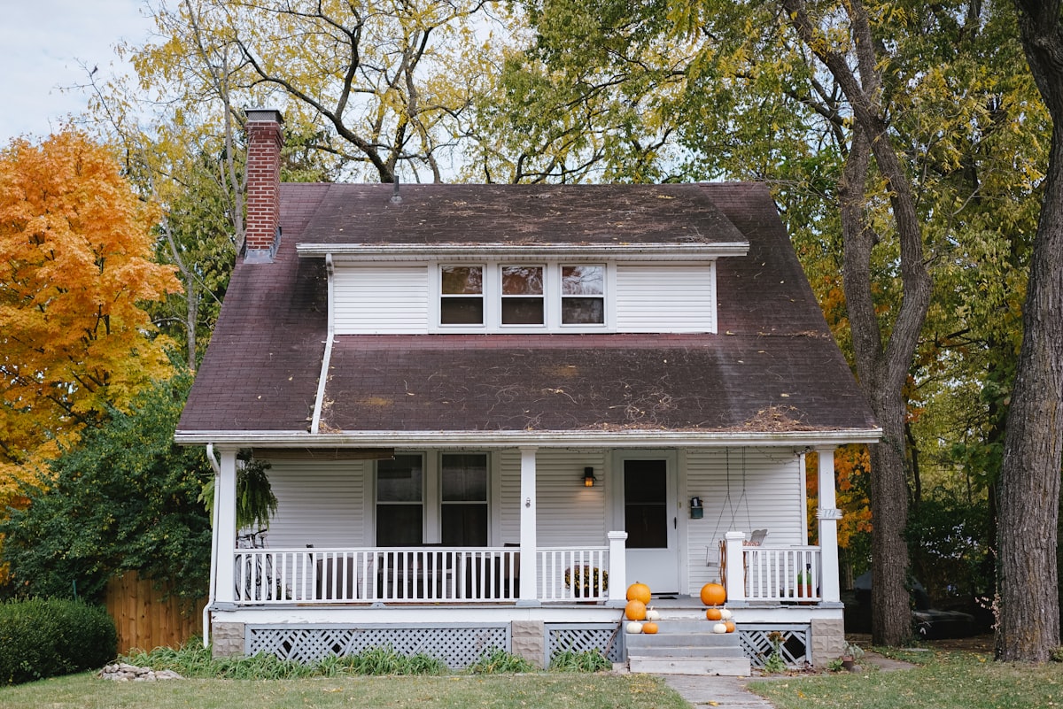 A white craftsman home with a wide front porch under autumn trees